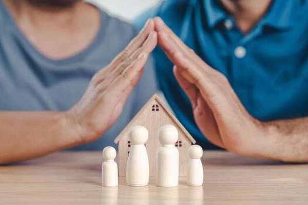 Hands protecting paper figures representing a family's health coverage